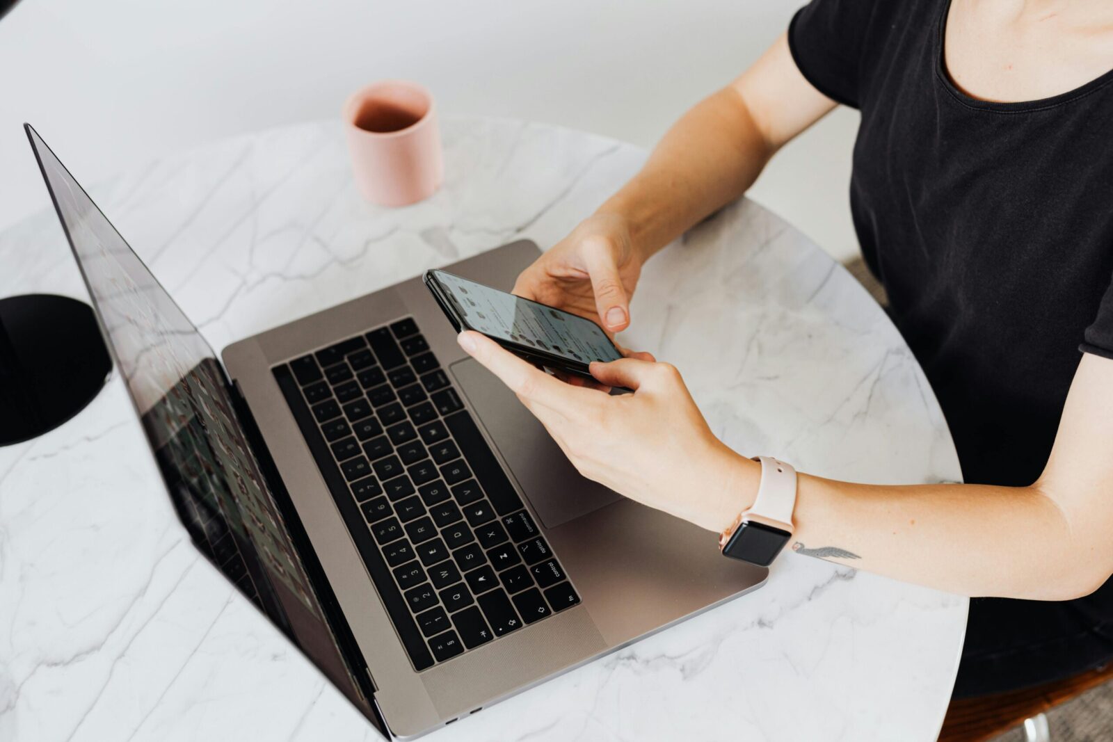 A woman interacts with her smartphone at a modern desk with a laptop, showcasing technology use.